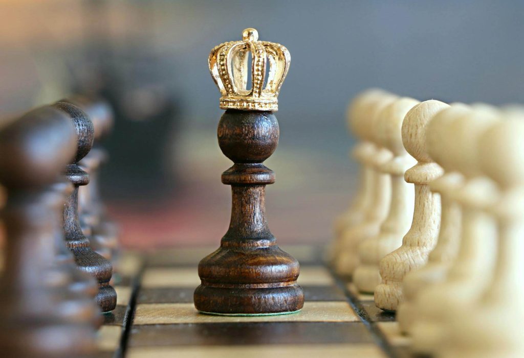 Image of a pawn wearing a crown with black and white pawns lined up on both sides on a chess board.