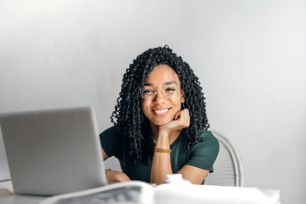 Image of a smiling woman sitting at a desk working on a laptop indicating that Sabbath rest meaning is related work but in a different way.